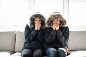 couple-sitting-with-parkas-on-in-living-room