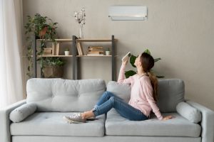 comfortable-woman-witting-on-couch-in-front-of-ductless-air-handler-holding-remote