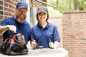 male-and-female-technician-standing-over-outside-ac-unit-with-tool-bag-and-tools